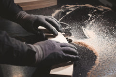 Gloved hands smoothing a timber board on a workbench covered in sawdust